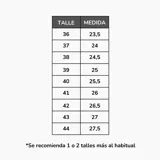 Zapatillas deportivas de estilo retro, color negro con detalles en beige claro y gris. Presentan una capellada de malla y superposiciones de material sintético, cordones negros y una suela gruesa con capas grises.