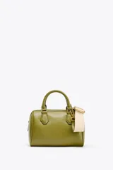 Bolso formato mini bowling color verde oliva con detalles metálicos dorados en las asas. Tiene doble asa de mano y correa bandolera extraíble. Incluye bolsillo interior con cremallera y cierre principal con cremallera.