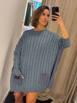 Sweater negro de punto con diseño de trenzas, corte holgado, mangas largas y bolsillos frontales. Tejido artesanalmente en Uruguay, con puños altos ajustados.