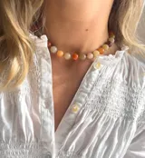 Gargantilla corta con cuentas redondas de piedra en tonos naranja, marrón, beige y blanco, unidas por pequeñas cuentas doradas.