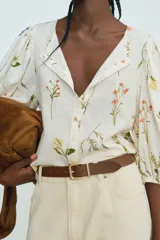 Blusa de lino color blanco con estampado de flores, cuello redondo, cierre de botones y mangas globo tres cuartos con puños elásticos.