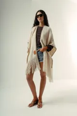 Ruana tejida a mano en lana merino 100%, de color marrón con detalles de costura en rojo en los bordes y terminación de flecos largos en el ruedo. Presenta una silueta amplia y caída natural, confeccionada artesanalmente por Manos del Uruguay.