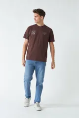 Remera marrón de algodón con cuello redondo, corte regular y estampado en el pecho. El modelo usa talle M.