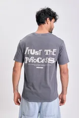 Remera de manga corta color gris oscuro con efecto gastado, cuello redondo y estampa grande en la espalda con el texto "TRUST THE PROCESS" y una frase motivacional debajo.