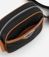 Cartera bandolera negra con detalles en marrón, confeccionada en poliéster certificado Grs y poliuretano. Presenta un aplique metálico triangular, asa larga ajustable y cierre por cremallera.