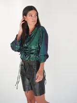 Camisa verde esmeralda con reflejos tornasolados, de corte holgado, con cuello camisero, cierre frontal con botones de nácar y mangas largas con puños abotonados.