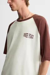 Camiseta blanca con mangas cortas marrones tipo ranglán, cuello redondo y estampado con la frase "Inner Peace" en marrón.