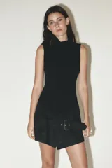 Mono corto negro con cuello alto y sin mangas. La parte inferior simula una falda cruzada con cinturón y hebilla metálica. Cierre trasero con cremallera oculta.