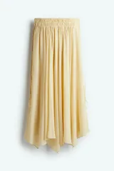 Pollera circular larga color amarillo pálido, de gasa transparente con viso corto. Presenta cintura alta con elástico, tiras finas largas en los laterales y bajo asimétrico con tajo pronunciado en los laterales.
