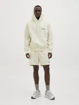 Buzo canguro color crema con capucha, mangas largas, puños de canalé, bolsillo canguro y estampado azul en la espalda con la leyenda "project core creative dept. unlimited edition sourced and produced by jack&jones® 1990".