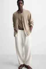 Pantalón blanco de corte relajado con pliegues frontales, bolsillos laterales y bolsillos traseros de vivo. Cierre frontal con cremallera y botón.