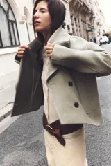 Abrigo corto color verde oliva, de cuello solapa y manga larga. Cuenta con bolsillos delanteros de vivo y cierre frontal cruzado con botones.