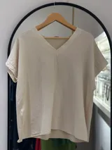 Remera beige de manga corta con cuello en V y calce holgado. La tela presenta una textura arrugada o con relieve.