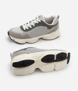 Championes dad sneaker grises con recortes en cuero sintético, cordones blancos y suela chunky de goma color crema.