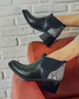 Bota corta de cuero sintético negro con elástico lateral y detalle de estampado animal print en el talón.