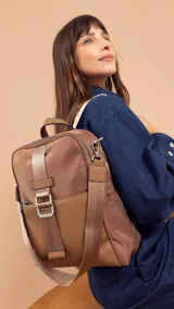 Mochila combinada de tela impermeable color marrón y simil cuero color marrón claro, con correa corta para usar como cartera. Incluye un bolsillo grande con cierre al frente y bolsillos laterales.