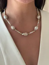 Collar corto de perlas de río alargadas y ovaladas, con cuentas de acero quirúrgico y bolitas con baño de oro. Cierre con cadena de acero quirúrgico y gancho para regular el largo.