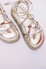 Sandalias de plataforma color dorado con tiras plateadas y cobrizas para atar alrededor del tobillo.