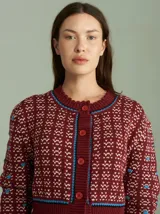 Cardigan de punto color borgoña con diseño geométrico en blanco y detalles en azul. Tiene cuello redondo, cierre frontal con botones rojos y mangas largas con puños acanalados.