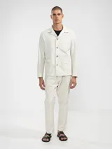 Pantalón de vestir color crema, confeccionado en tejido ligero de algodón con textura seersucker. Tiene corte recto, bolsillos laterales y traseros, cierre con botón y cremallera, y parche con logo de la marca.