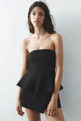 Top blanco de tejido elástico, sin mangas y con escote recto. Tiene corte peplum en la parte inferior y cierre con cremallera oculta en la costura.