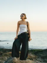 Pantalón negro de pierna ancha con cierre de gancho y cremallera, bolsillos laterales y detalle plisado.