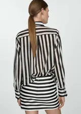 Camisa de manga larga con puños abotonados, cuello camisero y cierre frontal con botones. Diseño a rayas verticales blancas y negras sobre tejido semitransparente.