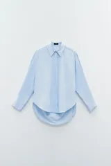 Camisa celeste con rayas verticales blancas, de corte clásico, con cuello camisero, cierre con botones y mangas largas con puños abotonados. El ruedo es redondeado y más largo en la parte trasera.