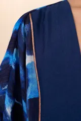 Kimono corto azul con estampado abstracto en tonos azules y blancos, con detalles dorados. Presenta mangas 3/4 amplias, cinturón liso y guarda frontal en color azul liso.