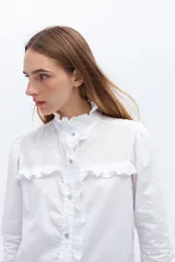 Camisa blanca de algodón con bordado calado, cuello alto con volados y cierre frontal con botones.