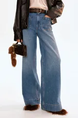 Pantalón de jean de algodón con leve stretch, tiro alto y pierna ancha. Presenta bolsillos de parche cuadrados en la parte delantera y bolsillos traseros. El lavado es celeste medio con efecto de desgaste vertical en las piernas.