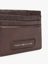 Tarjetero marrón de cuero con diseño de monogramas TH en relieve en la parte superior y logo metálico de Tommy Hilfiger en la parte inferior.