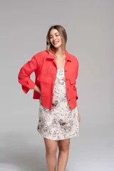 Campera corta color coral con cuello camisero, cierre frontal con botones, bolsillos de parche en el pecho y mangas largas con puños abotonados. Presenta calados tipo broderie en hombros, mangas y espalda.