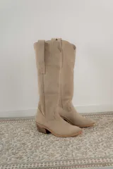 Bota alta de cuero color beige, estilo texana, con caña alta y taco bajo.