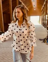 Camisa blanca con lunares negros, de corte holgado y mangas largas abullonadas con puños elásticos.