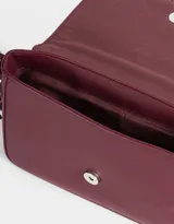 Bandolera color crudo de cuerina con solapa y correa regulable con hebilla. Incluye charm decorativo lateral y cierre con broche a presión.