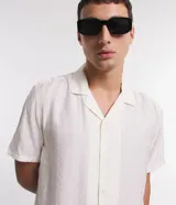 Camisa boxy de hombre confeccionada en viscolino color crudo con rayas texturizadas, cuello inglés, solapa, mangas cortas y abotonado frontal.