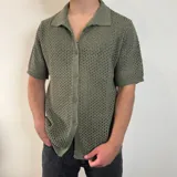 Camisa tejida de manga corta color verde oliva, con cuello tipo polo y cierre frontal con botones.