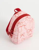 Llavero con forma de mochila pequeña color rosa claro con estampado de moños rojos y cierre con cremallera roja.