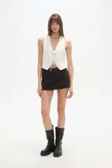 Chaleco blanco de algodón con escote en V profundo y cierre frontal ajustable mediante dos hebillas metálicas.