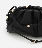 Cartera transversal pequeña color beige, confeccionada en material sintético con bretel fino de cordón con detalles de metal.