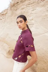 Blusa color camel con cuello mao, cierre frontal con botones y aberturas geométricas en hombros, mangas y cintura.