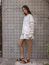 Buzo de algodón color blanco roto, de corte holgado, con puños y tajos laterales. Presenta un bordado artesanal en relieve de líneas orgánicas en color marrón caramelo sobre las mangas.