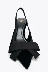 Zapato destalonado negro de terciopelo con tacón fino y tira trasera elástica. Detalle de lazo en la parte delantera.