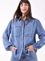 Camisa celeste de denim con dos bolsillos frontales con solapa y manga larga con puños abotonados.