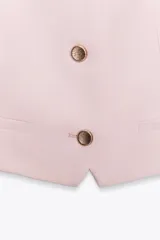 Chaleco amarillo pálido con cuello cuadrado, tirantes finos, falsos bolsillos de vivo y cierre frontal con botones.