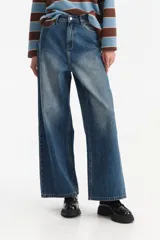 Jean de mezclilla azul con corte ancho y tiro medio, presentando un efecto desgastado en la parte frontal.