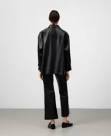 Sobrecamisa de cuero sintético color negro con cuello italiano y manga larga. Presenta cierre frontal de botones, un bolsillo de parche en el pecho, aberturas laterales y bajo redondeado con espalda ligeramente más larga.