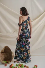 Vestido largo de satén de seda negro con estampado de flores de colores. Tiene escote irregular drapeado, un bretel ancho y otro fino con manga caída.