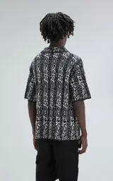 Camisa de manga corta tejida de punto abierto (símil crochet), calce oversize, color negro con diseño abstracto en beige.